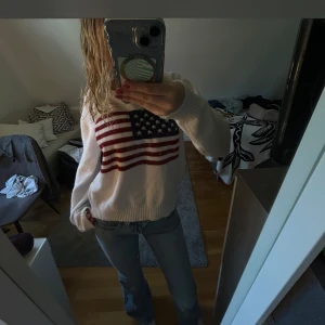 Vit stickad tröja med USA-flagga - Ralph Lauren doup, Vit stickad tröja med stor amerikansk flagga framtill i rött, blått och vitt. Tröjan har rund hals, ribbade muddar och lång ärm. Använt få gånger. 