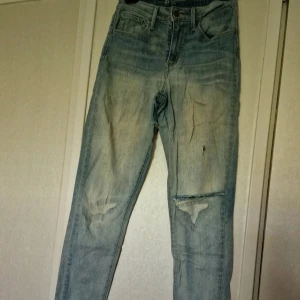 Levis 511 ljusblå slitna jeans - Ljusblå Levis 511 jeans med snygga slitningar och hål på knäna för en cool, avslappnad vibe. Klassisk femficksmodell med smal passform och låg midja. Jeansen har en tvättad look och är gjorda i mjukt denimtyg som sitter skönt hela dagen. Byxorna är inköpta med en sliten look. Efter mycket användning ser de än mer slitna ut. Det finns två fläckar vad jag har kunnat se, ett litet hål nedanför grenen, ett hål på vänster knä samt ett på vänster lår (se bilder). Stl W27 L34 