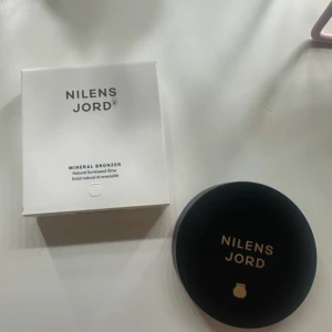 Nilens Jord Mineral Bronzer Pretty Glow - Mineral Bronzer från Nilens Jord i färgen Pretty Glow. Kompakt dosa med spegel och fyra sektioner: två skimrande bruna nyanser, en matt brun och en rosaröd ton. Fragrance free och innehåller 12 gram. Perfekt för att skapa en naturligt solkysst look.