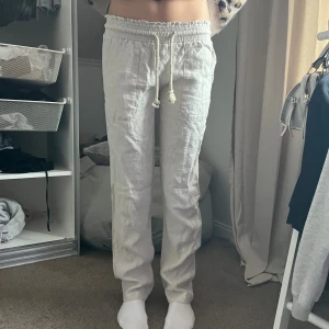 Linnebyxor med snörning i ljusbeige - Snygga och luftiga linnebyxor i ljusbeige med elastisk midja och snörning framtill. Byxorna har raka ben och en avslappnad passform, perfekta för en chill och stilren look. Materialet är linne som ger en skön känsla och andas bra.