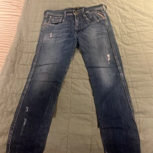 Blå Replay jeans med slitningar - Säljer ett par blå jeans från Replay med snygga slitningar och klassiska fem fickor. Jeansen har slim  passform, raka ben och detaljerade sömmar. Märkespatch bak i midjan.  Perfekta för en avslappnad och trendig look.