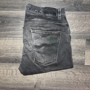Nudie Jeans - Säljer ett par svarta jeans från Nudie Jeans i storlek 36/34. Jeansen har en snygg tvättad look med klassiska fem fickor och raka ben. Materialet är jeans och de har en stilren, enkel design med diskreta detaljer. Midja 45cm, längd 112cm. JAG SKICKAR INGA FLER BILDER NÄR JAG BÄR JEANSEN:) s2 