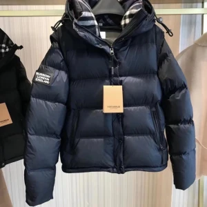 Burberry pufferjacka med huva - Snygg pufferjacka från Burberry med klassiskt rutigt foder i huvan och patch på ärmen. Finns i svart, mörkblå och beige. Jackan har dragkedja, knappar och justerbar huva. Perfekt för kalla dagar och riktigt trendig stil.