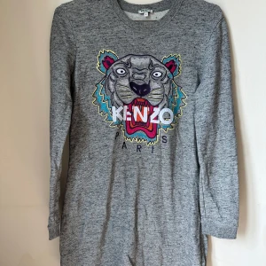 Grå sweatshirt klänning med tiger från Kenzo - Säljer en grå sweatshirt från Kenzo med ikoniskt broderat tigerhuvud i färgglada nyanser och logga på bröstet. Tröjan är långärmad, har rund hals och är tillverkad i mjuk 100% bomull. Perfekt för dig som gillar statement-plagg och streetstyle.