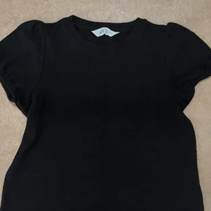 Svart kortärmad topp från H&M - En svart, enkel och stilren topp från H&M med rund halsringning och korta ärmar. Modellen är klassisk och passar perfekt till jeans eller kjol. Tillverkad i mjuk bomull för en bekväm känsla hela dagen. Perfekt till höst.