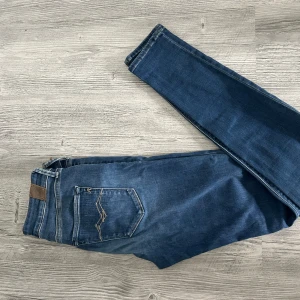 Blå Replay  jeans - Snygga blå jeans från Replay med klassisk femficksdesign och coola detaljer på bakfickan. Jeansen har normalhög midja, smal passform och är tillverkade i stretchigt denim för extra komfort. Perfekta för dig som gillar en stilren och modern look.