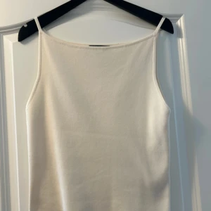 Vit linnetopp med smala axelband - Enkel och stilren vit linnetopp med smala axelband och rak halsringning. Tunt och mjukt material som känns skönt mot huden.