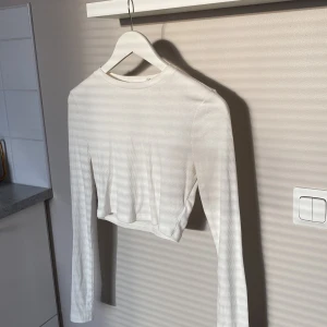 Vit croppad långärmad topp - NA-KD - Säljer en vit croppad långärmad topp från NA-KD i ribbad bomull, storlek S. Enkel och stilren design med rund halsringning och tight passform. 