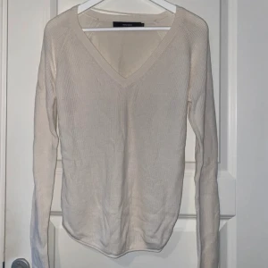 Beige v-ringad stickad tröja Vero Moda - Beige stickad tröja från Vero Moda i storlek XS. Tröjan har v-ringning, lång ärm och är ribbstickad för en snygg och enkel look. Perfekt att matcha med jeans eller kjol för en clean stil.