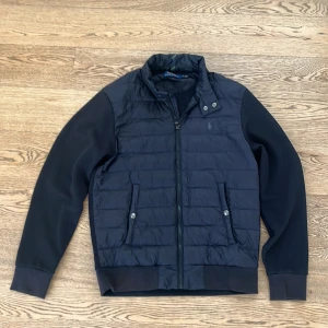  Polo Ralph Lauren cardigan svart - Säljer en svart cardigan från Polo Ralph Lauren med quiltad framsida och släta ärmar. Jackan har dragkedja, ståkrage med tryckknappar och två fickor framtill. 