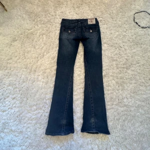 True Religion Joey Low Rise Flare Jeans - Nu säljer jag mina jätte fina Mörkblå jeans från True Religion, modell Joey Low Rise Flare. Snygga lågmidjade byxor med bootcut. Klassiska bakfickor med lock och dekorativa sömmar samt logopatch bak. Tillverkade i jeansmaterial med coola detaljer och knappar med logga. Några pärlor har dock tyvärr trillat av vilket man ser på sista bilden. De kostar 900kr + frakt som kunden betalar, pris kan diskuteras 