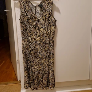 Blommig långklänning från Lindex - Supersnygg långklänning från Lindex i storlek S. Klänningen är ärmlös med v-ringad hals och har ett blommigt mönster i svart, vit och gul. Materialet är mjukt och lätt, perfekt för varma dagar. Passformen är normal och klänningen har en fin siluett som faller snyggt.