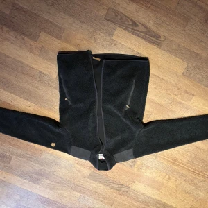 Mörkgrön teddyjacka från Fjällräven S - Mysig mörkgrön teddyjacka från Fjällräven i herrmodell. Jackan har hel dragkedja, två fickor med dragkedja och förstärkta partier på armbågar och axlar. Klassisk Fjällräven-logga på ärmen och skön fleece-känsla. Perfekt för kyliga dagar.