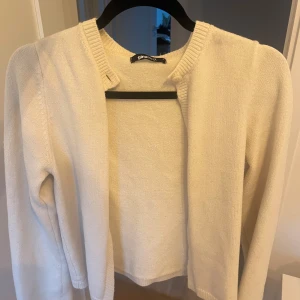 Beige kofta från Gina Tricot - En stilren beige kofta från Gina Tricot i mjukt stickat material. Koftan har rund halsringning, ribbade muddar och lång ärm. Perfekt att slänga över en topp för en enkel och clean look.