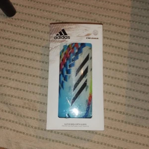 Adidas benskydd X League rainbow färg - Säljer ett par Adidas X League benskydd med färgglad design i blått, svart, rött och gult. Snygga grafiska mönster och klassiska Adidas-ränder. Perfekta för att inte skada benen vid kollision. Mjukare på insidan och hållbart skal.