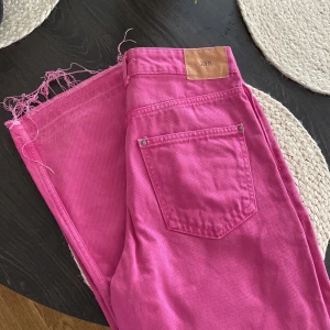 Rosa jeans från Zara, strl 36 - Snygga rosa jeans från Zara i storlek 36. Modellen är högmidjad med raka ben och råa, fransiga benslut. Klassisk femficksdesign och tillverkade i bomull. Använda endast 1 gång och är långa! (Är 177cm lång)