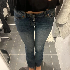 Lågmidjade jeans från Junkyard - Säljer ett par snygga blå bootcut jeans från Junkyard med klassisk femficksdesign och cool kontrastsöm på bakfickorna. Jeansen har låg midja och är gjorda i ett slitstarkt bomullsmaterial. Perfekta för dig som gillar en retro vibe och vill ha ett par jeans med lite utsvängda ben.