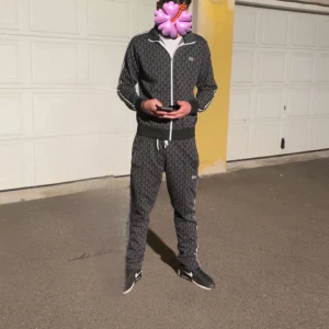 Lacoste tracksuit  - Säljer en svart ziptröja från Lacoste med hel dragkedja och vit piping längs dragkedjan och ärmarna. Tröjan har ett diskret mönster med Lacoste-loggor över hela och klassisk ståkrage. Tillverkad i bomull och polyester, perfekt för en sportig och clean look. Äkta man kan skanna storlek s men passar m 