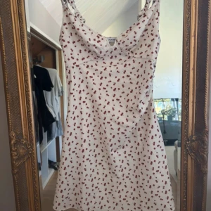 Vit kort klänning med körsbär från ADOORE - Supersöt vit kort klänning från ADOORE med röda körsbär över hela tyget. Klänningen har rynkade axelband och en lätt v-ringad urringning. St L