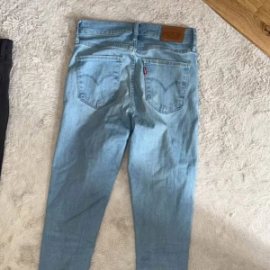 Levi's ljusblå skinny jeans - Ljusblå jeans från Levi's med klassiska bakfickor och röd logotagg. Modellen har smal passform och hög midja. Perfekta för dig som gillar en clean och enkel look. Tillverkade i mjukt jeanstyg som sitter snyggt hela dagen. Nyskick, storlek 25.