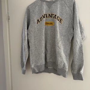 Grå sweatshirt från Björn Borg - Säljer en grå sweatshirt från Björn Borg med trycket 'ADVANTAGE' i svart och gult på bröstet. Tröjan har rund hals, långa ärmar och ribbade muddar. Perfekt för en sportig och avslappnad stil. Har en liten defekt på den högra armen, kolla bild