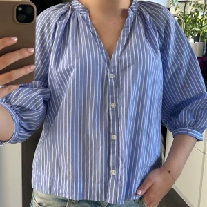 Blåvit randig skjorta från H&M - Säljer en blå och vit randig skjorta från H&M i storlek S. Skjortan har v-ringning, knappar framtill och trekvartsärmar med resår vid ärmslut. Den är i luftigt bomull och har en loose fit som ger en chill look i vardagen💙🤍💙