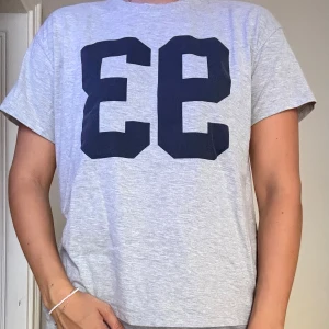 Grå t-shirt med blå tryck - Klassisk passform och rund halsringning, perfekt för en avslappnad stil. 