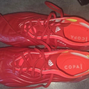 Röda Adidas Copa Sense fotbollsskor - Säljer ett par röda Adidas Copa Sense skinn fotbollsskor med snörning och vågformade detaljer. Skorna har en syntetisk ovandel och dobbar i gult och vitt på sulan. Storlek 44