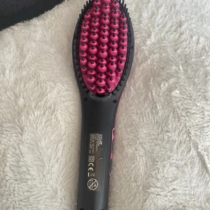 Platt Värmeborste - En svart och rosa elektrisk hårborste med värmefunktion. Borsten har en oval form och är utrustad med knappar för att justera temperaturen. Perfekt för att snabbt styla håret och få det slätt. Ansluts med vanlig EU-kontakt. Från girl it
