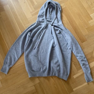 Ljusgrå hoodie med snörning - En stilren ljusgrå hoodie med snörning i huvan och ribbade muddar. Tröjan har en klassisk passform och är tillverkad i mjukt bomullsmaterial, perfekt för chill dagar. Långärmad och enkel att matcha med jeans eller joggers.