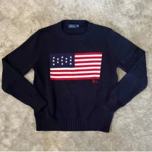 Mörkblå stickad tröja Polo Ralph Lauren - Snygg mörkblå stickad tröja från Polo Ralph Lauren med amerikansk flagga i rött, vitt och blått på bröstet samt RL-broderi. Rund hals och ribbade muddar vid ärmslut och nederkant. Perfekt för dig som gillar klassisk och cool stil. Fick den som present men den är tyvärr förliten, har inget kvitto så gick inte att lämna tillbaks så säljer för en snabb peng