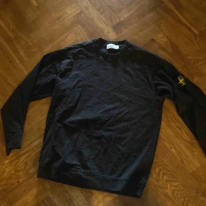 Svart långärmad tröja från Stone Island - Svart långärmad tröja från Stone Island med klassisk rund hals och ikonisk logotyp-patch på vänster ärm. Tröjan är i mjuk bomull och har en clean, stilren look som passar perfekt till streetwear. Snygg och enkel att matcha med jeans eller cargo. Säljs eftersom den inte passar mig längre! 