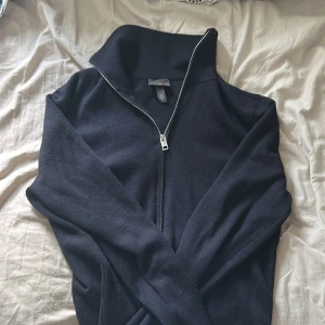 Mörkblå stickad half zip-tröja H&M - Mörkblå stickad tröja från H&M. Långärmad och i mjukt material som passar perfekt till lager-på-lager. Enkel och stilren design som funkar till många outfits. Liten defekt längst ner på tröjan som enkelt går att fixa