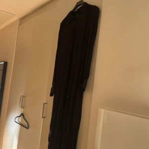  långklänning från Linindex svart - Säljer en långklänning i svart från Lindex. Klänningen har långa ärmar, klassisk krage och knappar hela vägen framtill. Materialet är mjukt och flowy, perfekt för dig som gillar en avslappnad men ändå stilren look.