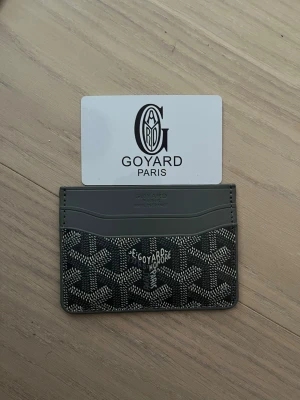 Grå plånbok med mönster - Säljer en stilren svart plånbok med deras ikoniska grafiska mönster. Plånboken har flera kortfack och är tillverkad i skinn med detaljer i syntet. Perfekt för dig som vill ha något exklusivt och snyggt i fickan.