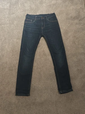 Mörkblå slim fit jeans - Säljer ett par mörkblå slim fit jeans med klassisk femficksdesign och smal passform. Jeansen har normal midja och är tillverkade i stretchigt denimtyg för extra komfort. Perfekta till sneakers eller boots och funkar året runt. Riktigt bra för dig som är Grisch. Skick 8/10 bara använts några fåtal gånger. Nypris 399kr