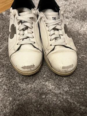 Vita sneakers The Gallerist med svart detalj - Snygga vita sneakers från The Gallerist med svart häl och grå klubb-symbol på sidan. Skorna har snörning, platt sula och är gjorda i skinn. Perfekta för dig som gillar en clean look med en twist. Sulan är beige och ovandelen har slitna detaljer för en cool vibe. omhändertagna. Passar perfekt både till vardag och mer uppklädda outfits. De är använda en höst och nytt pris är 2699. Pris kan diskuteras!