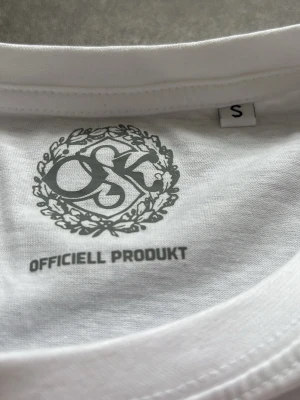 Vit Örebro SK t-shirt signerad - Vit t-shirt från Örebro SK med tryck fram i svart, grönt och rött. Framsidan har klubbens logga och texten 'Örebro Sportklubb 1908'. Baksidan är täckt av autografer och årtalet 2023. Klassisk passform och mjukt bomullsmaterial. Har aldrig använts eller tvättats så alla autografer är i nytt skick.