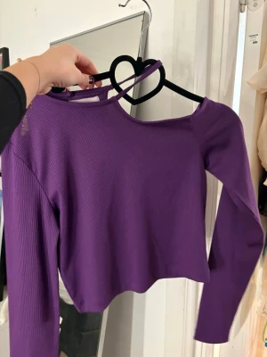 Lila ribbad croppad topp - Säljer en lila croppad topp med lång ärm och ribbad struktur från lefties. Toppen har en unik asymmetrisk halsringning med en extra axelrem som ger en cool twist. Perfekt för dig som vill sticka ut lite extra.
