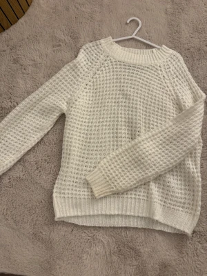 Vit stickad tröja - Säljer en vit stickad tröja i storlek XS med ribbade muddar vid hals, ärmslut och nederkant. Tröjan har långärmad passform och ett luftigt stickat mönster som ger en mysig vibe. 