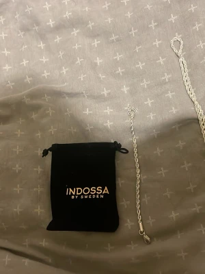 Ingen väst på bilderna - Bilderna visar ett silvrigt halsband från Indossa by Sweden med tillhörande svart tygpåse. Ingen väst syns på bilderna.