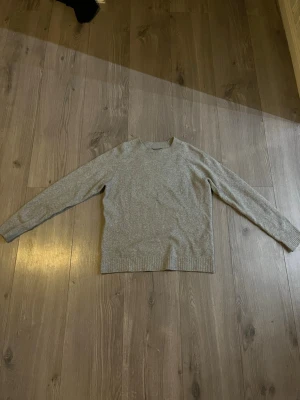 Grå stickad tröja med rund hals - En enkel och stilren grå stickad tröja med rund halsringning och långa ärmar. Perfekt att slänga på sig när det är kyligt ute. Tröjan har ribbade muddar vid ärmslut och nederkant för en snygg passform.