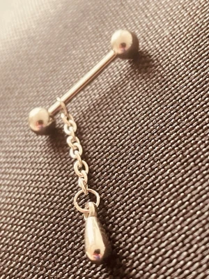 By prisförslag- Silverfärgad barbell med droppe och kedja  - Snygg barbell-piercing i silverfärgad metall med två kulor och en hängande kedja med droppformad detalj. Perfekt för dig som vill ha en lite extra edge på din look. Stilren och minimalistisk design som passar till många stilar.