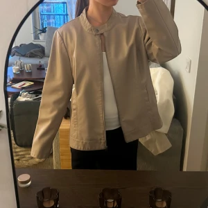 Beige skinnjacka - Säljer en stilren beige skinnjacka från only med rak passform och ståkrage. Jackan har dragkedja framtill, knapp vid halsen och två fickor på sidorna. Perfekt till vår och höst för en clean look. Jackan är sparsamt använd och i nyskick!💕Det står storlek 46 men jag skulle säga att den passar S/M om man vill ha en oversized look