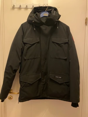 Svart vinterjacka Canada Goose Constable Herr - Säljer en svart Canada Goose Constable vinterjacka med fyra stora fickor framtill, huva med dragsko och klassisk röd logga på ärmen. Jackan är vadderad och har dragkedja framtill. Perfekt för kalla dagar och riktigt snygg streetstil. Jackan har ej använts på över 10+ år och är därför i bra skick men tyget har fått lite missfärgning (se bild för detaljer). Jackan är kemtvättad. Pris kan diskuteras!