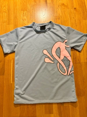 Ljusblå t-shirt med rosa print - Snygg ljusblå t-shirt med stort rosa grafiskt tryck både fram och bak.