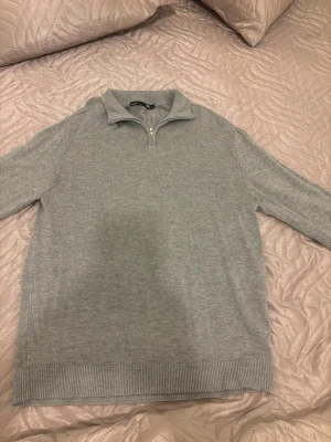 Quarter-zip - Snygg grå stickad tröja från 157 med halv dragkedja och hög krage. Perfekt för lager-på-lager och chill dagar. Ribbstickade muddar vid ärmslut och nederkant ger en clean look.