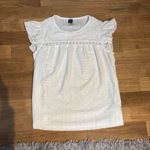 Vit blus med spetsdetaljer  - Supersöt vit blus från shein  med broderade hålmönster och volangärmar. Blusen har en fin spetskant med små blommor över bröstet och är tillverkad i bomull. Perfekt för en fräsch och somrig look!