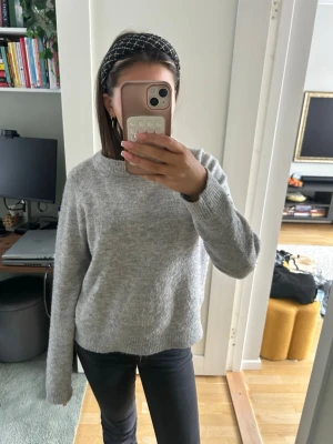 Grå stickad tröja från Vero Moda - Mysig grå stickad tröja från Vero Moda i storlek S. Tröjan har en klassisk rund halsringning och långa ärmar med ribbade muddar. Perfekt för lager-på-lager och chill dagar. Enkel att matcha med jeans eller kjol.