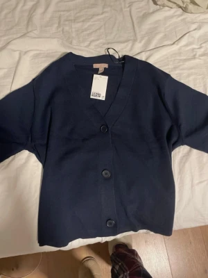 Finstickad kofta från H&M, storlek S - Säljer en mörkblå kofta från H&M i storlek S. Koftan har v-ringning, stora knappar framtill. Ganska lös i passform, väldigt skön och luftig! Inte använd, bara testad!! 